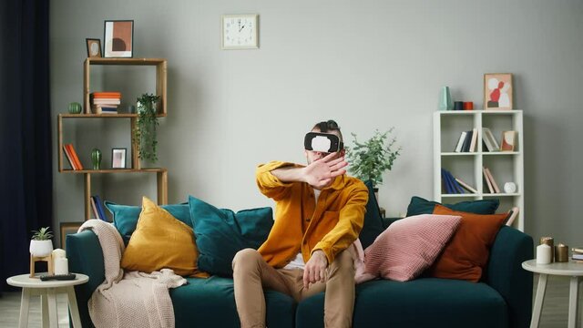 Man wearing vertual reality glasses, playing vr video game. Student enjoying AR 3D education learning video games in living room. Entertainment during home isolation covid lockdown.