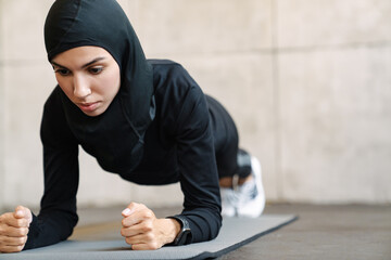 Young muslim woman in hijab doing exercise while working out indoors