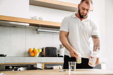 White man in eyeglasses holding medicine jar while standing at kitchen