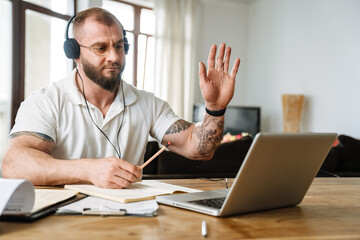 White man in headphones gesturing while working with laptop at home