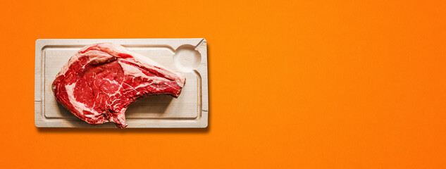 Beef prime rib and wooden cutting board isolated on orange background. Horizontal banner