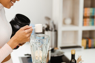 Black woman in headphones making smoothie with protein at home