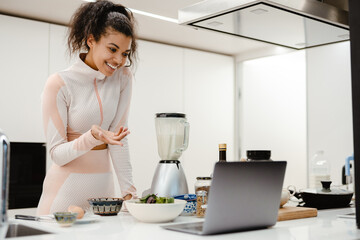 Black woman gesturing and using laptop while cooking