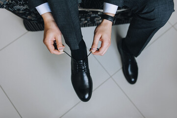 A man, a businessman, ties long shoelaces on leather black shoes, shiny with cream, with his hands in a jacket close-up. Advertising photography.