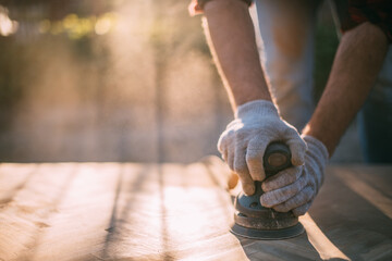 A male carpenter works with a wood grinder. Close-up. Professional equipment and protective equipment.