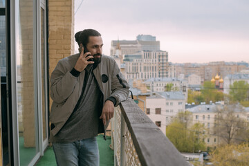 Portrait of a young handsome man with a phone on the balcony overlooking the city.