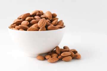 Almond nuts in a white bowl on isolate white background with nuts around the bowl.selective focus.front view. - Powered by Adobe