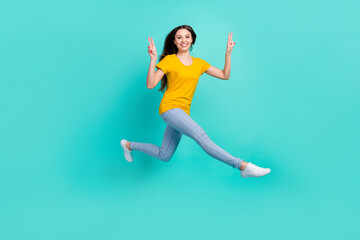 Fototapeta na wymiar Full size profile photo of funny young lady jump show v-sign wear yellow t-shirt jeans isolated on teal color background