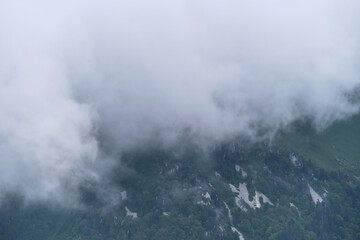 Obraz premium Forest and mountains in fog in cloudy weather. Beautiful landscape of National Park of Russia. Dark thundercloud envelops green mountain peak with coniferous forest.