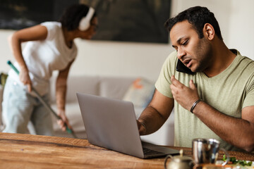 Middle eastern man talking on mobile phone while working with laptop