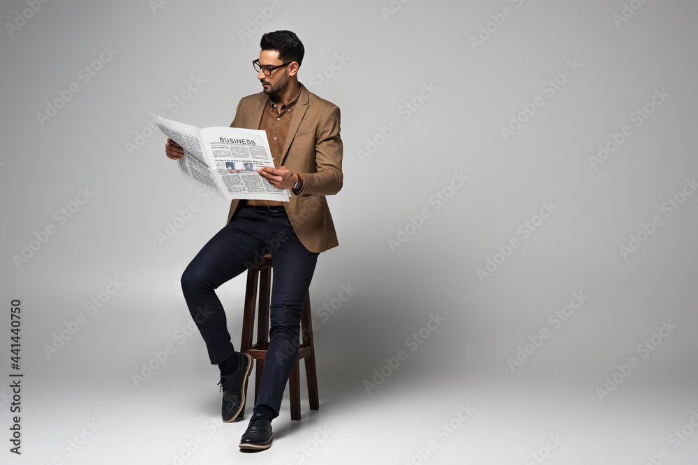 Poster good looking muslim businessman reading news on chair on grey background