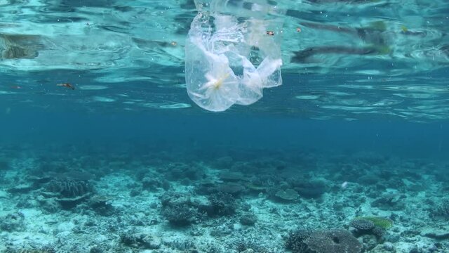 Plastic in the open ocean. Plastic bag with other trash floating over tropical coral reef.