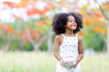 Childhood and explorer concept - A small curly haired African American girl holding a flower camera.