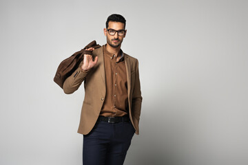 Fototapeta premium Muslim businessman in eyeglasses holding handbag on grey background