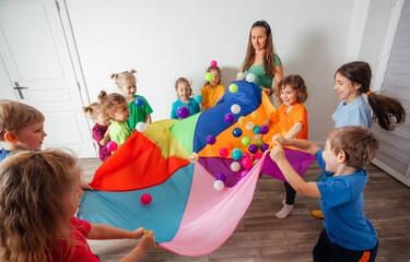 Schoolchildren playing using parachute with friends in gym