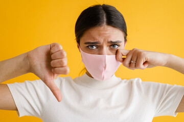 Young brunette woman in face mask crying and showing thumb down