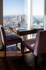 served table with armchairs in a restaurant or cafe with a panoramic window overlooking modern city buildings and the sea on a sunny day