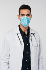Arabian doctor in medical mask looking at camera isolated on grey