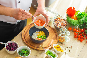 Young prepares a poke bowl in a modern kitchen. The man prepares food at home. Cooking healthy and...