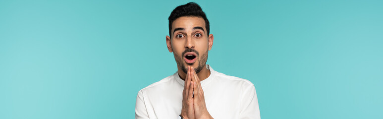 Amazed arabian man looking at camera and showing paying hands isolated on blue, banner