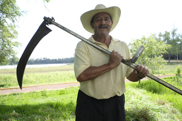 Hispanic male farmer with an old scythe for cutting weeds on a farm