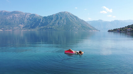 AERIAL. Young women enjoy floating on a mattress at the sea. Mountains on background.