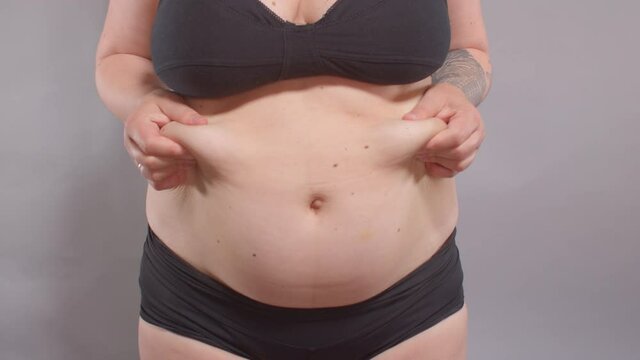 Fatty deposits on the abdomen of a woman after childbirth. She touches the folds of fat with her hands, lifts them. Stretching the skin during weight gain. Increase body volume.