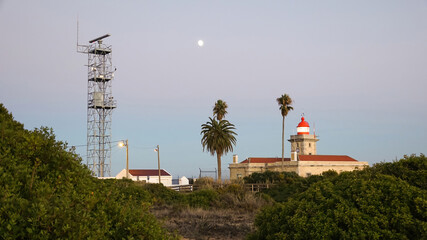 Lighthouse lit at sunset with radar communications tower and moon in the sky, Portugal