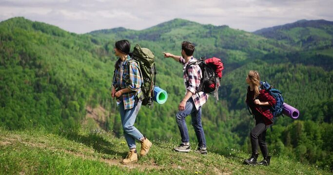 Group of three friends hikers walking relaxed in picturesque mountain area, enjoying backpacking tour, feeling excited about the trip. Travelling and tourism concept.