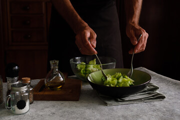 a man prepares a vegetable salad on a dark background. Dark photo style. It is transferred to a dish for serving on the table