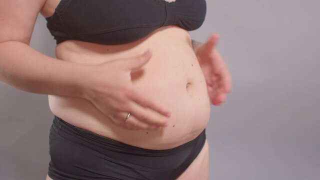 A woman touches her stomach with her hands, stretching the skin from adipose tissue. Body positivity, self-esteem enhancement. Weight loss motivation.