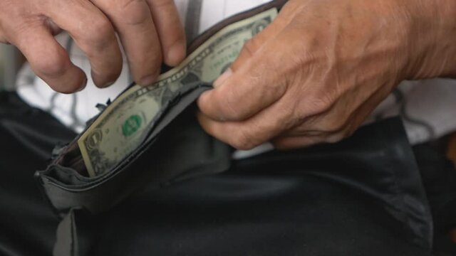 Elderly man's financial crisis and bankruptcy concept. Close-up of an old man's hand opening a torn shabby wallet from which he takes out a dollar bill. Selective focus