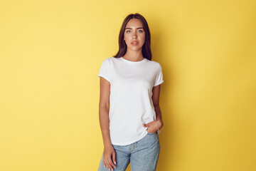 Attractive young woman in a white t-shirt stands on a bright yellow background.