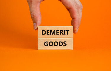 Demerit goods symbol. Wooden blocks with words Demerit goods on beautiful orange background, copy space. Businessman hand. Business and demerit goods concept.