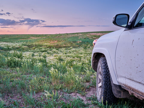 muddy SUV car or truck is riding at dusk through a green prairie - Pawnee National Grassland in northern Colorado, early summer scenery with wildflowers.