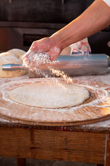 a guy making pizza sprinkling flour in the dough 