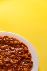 Traditional Hot chili sauce. Chopped meat, white beans, korn pepper, paprika in a tomato sauce. on a white plate and a yellow background