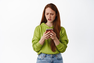 Disappointed teenage girl looking upset at smartphone application, dislike something at her phone,...