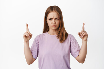 Portrait of moody young woman pointing up, furrows, frowning eyebrows upset, need explanation,...