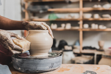 close up view of young african american man holding sponge and making wet clay pot on wheel in pottery - obrazy, fototapety, plakaty