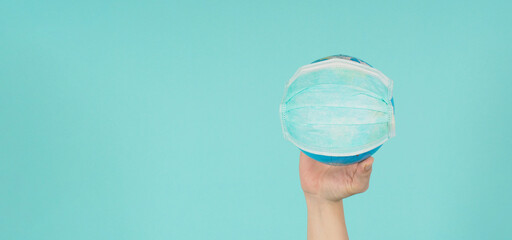 Hand is holding earth globe and face mask on green or Tiffany Blue background.covid-19 concept.