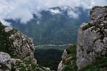 Natural window made of stones in mountains. Look into crevice in steep cliff and see dense green forest below. Nature and landscape of national Park in Caucasus in cloudy weather.