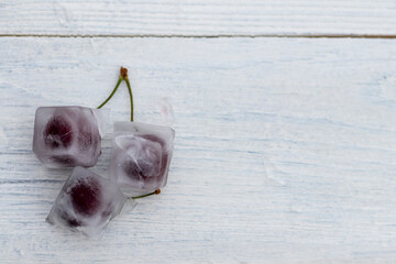 White wooden background in retro style. Red cherries in ice cubes. Close-up.