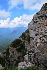 Nature and landscape of national Park in Caucasus. Cold summer day in mountains. Steep rocky mountain against background of snow capped mountains in distance on horizon.