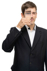 Young handsome tall slim white man with brown hair with glass of water in front of his eye isolated on white background