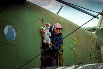 A middle-aged man with a dog aboard an old abandoned Soviet plane. The man gets out of the plane.