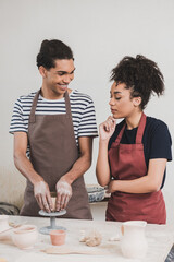 smiling young african american man making clay pot near woman with hand near face in pottery