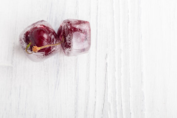 White wooden background in retro style. Red cherries in ice cubes. Close-up.