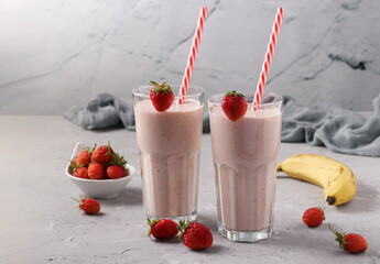 Homemade smoothie with strawberries and banana in two glass with drinking straw on gray background