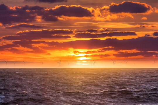 Renewable green electricity wind power generation offshore. Sunrise at decarbonization industry windmills business for regenerative energies. Clean energy renewables preventing climate change